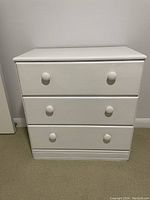 Image showing front view of small white dresser with three drawers and round knobs.