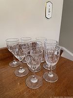 Eight clear crystal liqueur glasses arranged closely on a wooden surface, showing etched star pattern on bowl and sturdy round bases.