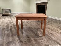 Rectangular wooden table viewed from the front showing natural wood grain and straight legs on a wood floor.