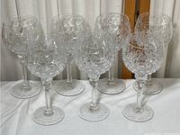 Seven clear Rogaska Gallia wine goblets with detailed cut crystal patterns, standing on a white cloth surface.