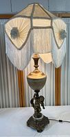 Full photo of the ornate table lamp showing the white fringed shade and cherub base.