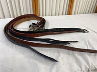 Photo showing multiple belts including brown smooth leather, black smooth leather, and braided brown leather, with metal buckles.