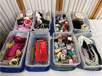 Full view of several plastic containers with sewing and crafting supplies including ribbons, threads, scissors, elastic, and fabric glue.