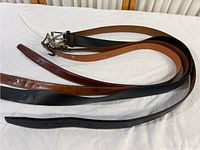 Three leather belts in different shades of brown and black laid out to show length and buckles.