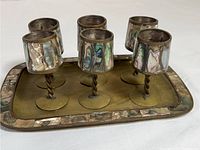 Full view of six vintage brass footed cordial glasses with mother of pearl inlay on a matching brass tray with mother of pearl border.