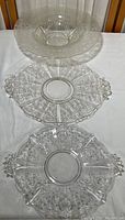 Three vintage clear glass serving dishes displayed on table showing elevated dish on top and two flat dishes below
