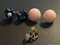 Photo showing 3 pairs of vintage Art Deco earrings on black background: black and turquoise geometric pair, large round pink clip-ons, small gold-tone clip-ons with clear beads.