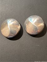 Pair of round sterling silver clip-on earrings on a black surface, displaying the front smooth and slightly domed surface with Art Deco style line details.