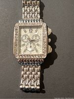 Silver tone rectangular vintage wristwatch with linked metal bracelet and rhinestones around the face on a dark background.