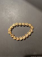 Gold tone heart-link lady bracelet with a small clear stone inside each heart shape, shown fully linked and laid flat.