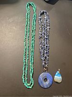Photo of three costume jewelry pieces: a green turquoise chip necklace, a blue sodalite chip necklace with a lapis lazuli donut pendant, and a teardrop-shaped banded agate pendant.
