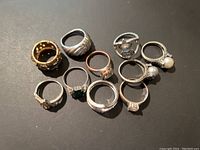 Ten assorted silver tone rings arranged showing various styles, stones and textures under neutral lighting