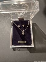 Set of necklace and earrings with clear zirconia stones in silver tone metal shown in a clear plastic display case with black velvet base.