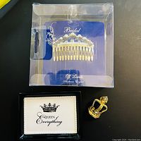 Bridal hair comb with clear crystals in a plastic box, gold-tone crown pin beside a card reading 'Queen of Everything'.