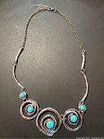 Top view of the unique artistic silver tone necklace showing three turquoise stones set within concentric circular frames and chain closure.
