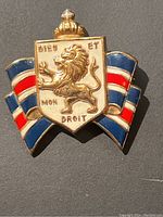Close-up front view of vintage British WWII pin with lion, crown, and red/white/blue enamel ribbons.