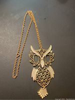 Full view of gold-tone owl pendant necklace on dark background