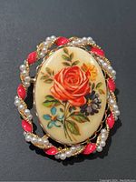 Close-up photo of the vintage rose hand painted brooch showing detailed floral artwork and decorative pearl and enamel border.