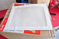 Single 9 x 12 inch white envelope with large transparent window placed on top of cardboard shipping box.