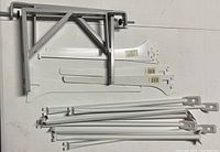 Large silver metal triangular bracket, white L-shaped brackets, and white rod-shaped brackets spread on a surface