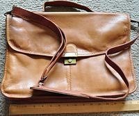 Front view of the brown leather satchel showing the adjustable shoulder strap and brass lock closure on the flap.