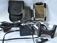 Full view of Compaq iPAQ H3800 Pocket PC and included accessories such as protective carry case, power adapter, USB cable, and charging cradle on white background.