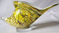 Side angle view showing the swirling yellow, green, and black colors with clear glass contours of the conch shell.