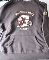 Front view of brown hoodie with embroidered Grumpy patch on chest showing Walt Disney World text and character G37 with kangaroo pocket.