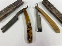Two straight folding razors laid out side by side with their original storage boxes. The razors are open to show their blades and handles, which show wear from use.