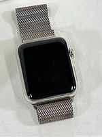 Front-facing view of silver Apple Watch with black screen and Milanese loop band laid out showing mesh texture.