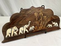 Full view of the carved wood plaque showing the shape, wood grain, and inlaid elephant and tree design.