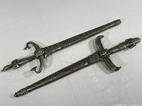 Two miniature metallic swords with Egyptian motifs laid side by side