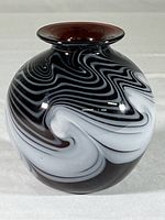 Front and side views of the hand-blown art glass vase with black and white swirls against deep amethyst background and flared rim.