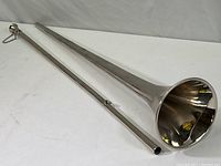 Full view of two pieces of steel no-valve trumpet laid out separately showing the long detachable tube and bell section.