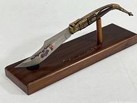 Full view of decorative cutter mounted on wooden stand showing ornate blade and handle