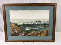 Framed watercolor painting showing full artwork of coastal waves and rocky shoreline, with blue matte and brown wood frame.