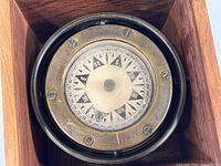 Close top-down view of the gimbal mounted compass showing dial and directional markings, with brass bezel and screws securing it.