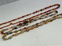 Three stone bead necklaces with different bead shapes and colors arranged on a white surface
