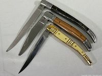 Three folding pocket knives laid side by side, showing handles and blades extended.
