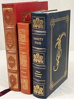 Three Easton Press classic books vertically standing showing leather bound covers of Vanity Fair (blue), Walden (orange), and The Red and the Black (red)