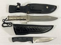 Two hunting knives with their leather sheaths laid flat, showing handles and blades.