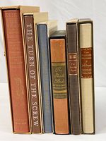Six classic novels in protective cardboard sleeves standing upright, spines visible. Titles visible: The Iliad, The Turn of the Screw, The Wind in the Willows, The Sketch Book, The Coverley Papers, The Pilgrims Progress.