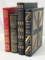 Four leather bound novels standing upright showing covers and spines, detailed gold embossing and coloring on leather visible.