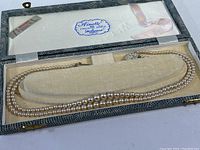 Full view of the double strand simulated pearl necklace displayed inside original hinged box with inner lid label, pink ribbon and textured reptile-patterned exterior.