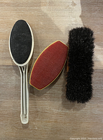 Top view of three brushes on a wooden surface: one shoe brush with black bristles, two lint brushes with red fabric cleaning surfaces.