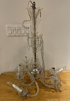 Crystal glass chandelier and sconce on wooden table, showing curved arms and hanging crystals, details of candle-style light sockets and plastic covers visible
