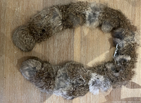 Overview of the brown fur scarf laid flat on wood surface showing its full length and tie ends.