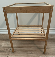 Front view of the side table showing glass top and wooden frame, slatted lower shelf visible.