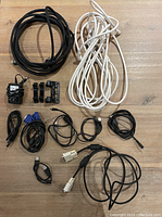 Top-down photo showing a variety of black and white miscellaneous cables and adapters laid out on a wooden surface.