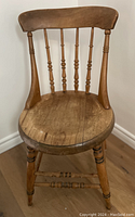 Front view of the round seated wooden chair showing the curved backrest with spindles and the worn round seat.